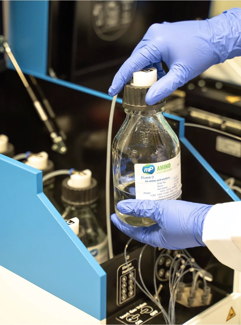 A technician in gloves holds a bottle labeled "Eluent D" while interacting with the ARACUS amino